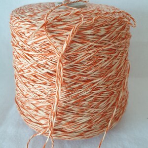 May include: A spool of orange and white striped yarn. The yarn is wound tightly around the spool and is ready to be used for knitting or crocheting.