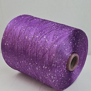Könnte beinhalten: Eine Spule mit violettem Garn, in das kleine, klare Pailletten eingewebt sind.