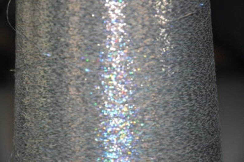 May include: Close-up of a silver metallic spool of thread with a shimmering iridescent sheen.