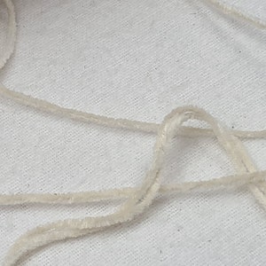 May include: A close-up of a white, fluffy yarn or string. The yarn is loosely coiled and tangled on a white surface.