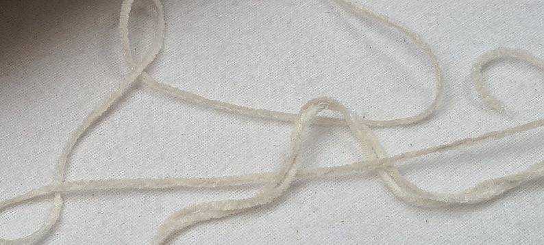 May include: A close-up of a white, fluffy yarn or string. The yarn is loosely coiled and tangled on a white surface.