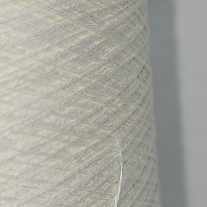 May include: A close-up of a spool of white yarn. The yarn is tightly wound and has a slightly textured surface.