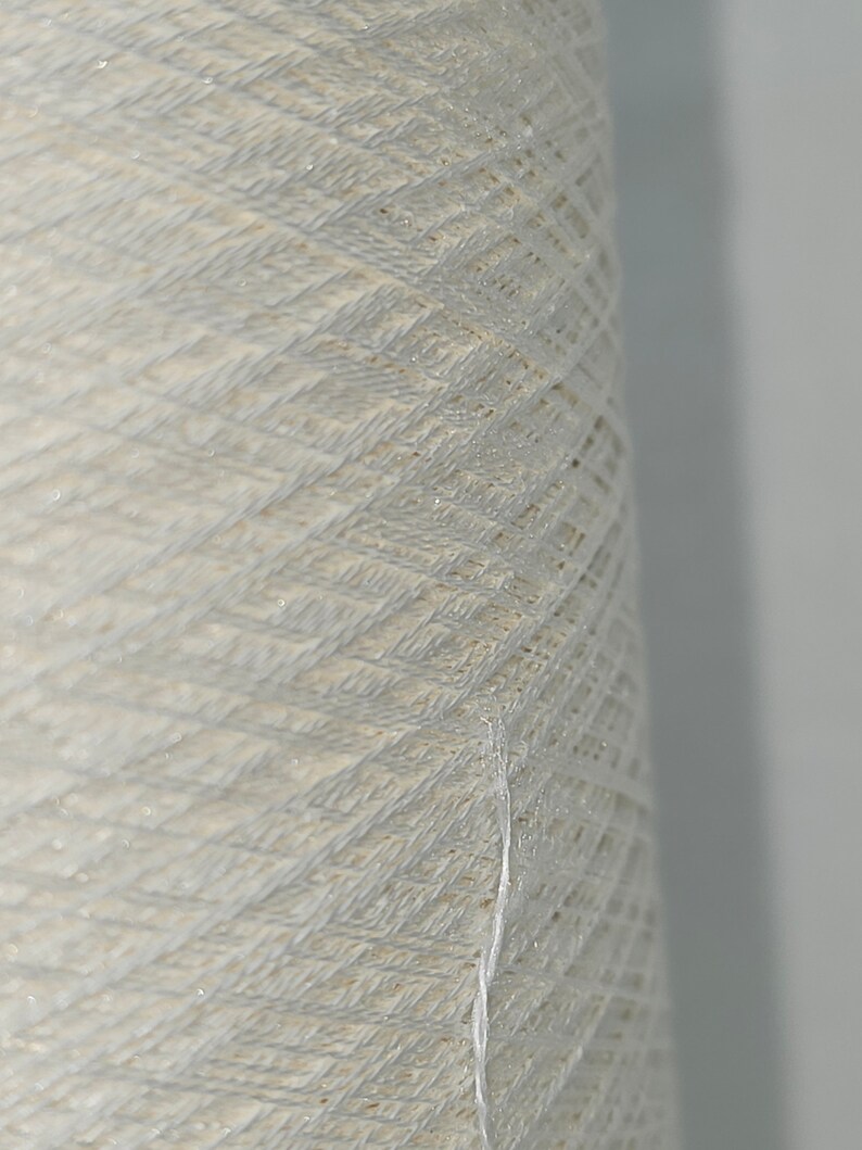 May include: A close-up of a spool of white yarn. The yarn is tightly wound and has a slightly textured surface.