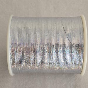 May include: A spool of silver metallic thread with a slight iridescent sheen.