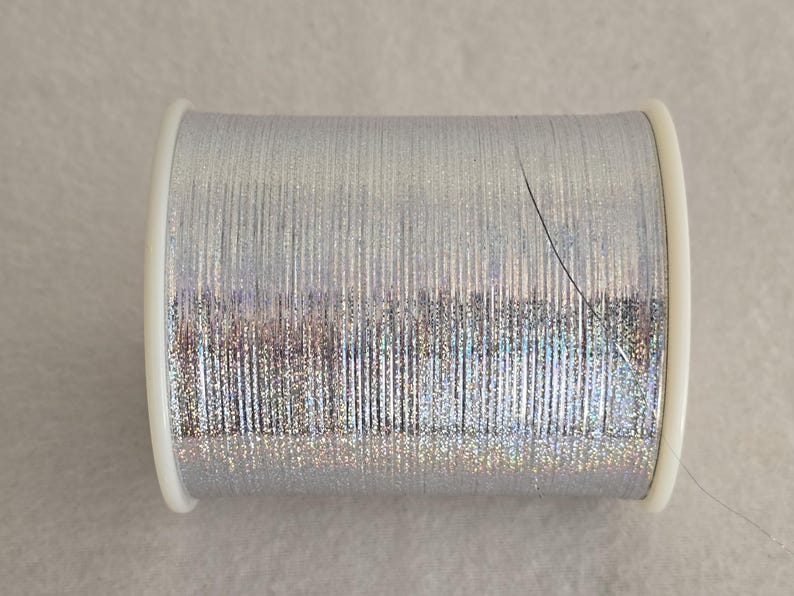 May include: A spool of silver metallic thread with a slight iridescent sheen.
