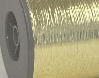 May include: Close-up of a spool of metallic gold thread. The thread is tightly wound around a gray plastic spool. The gold thread has a shiny, reflective surface, and the spool is partially visible.