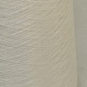 May include: A close-up of a spool of white yarn. The yarn is tightly wound and has a smooth, even texture.