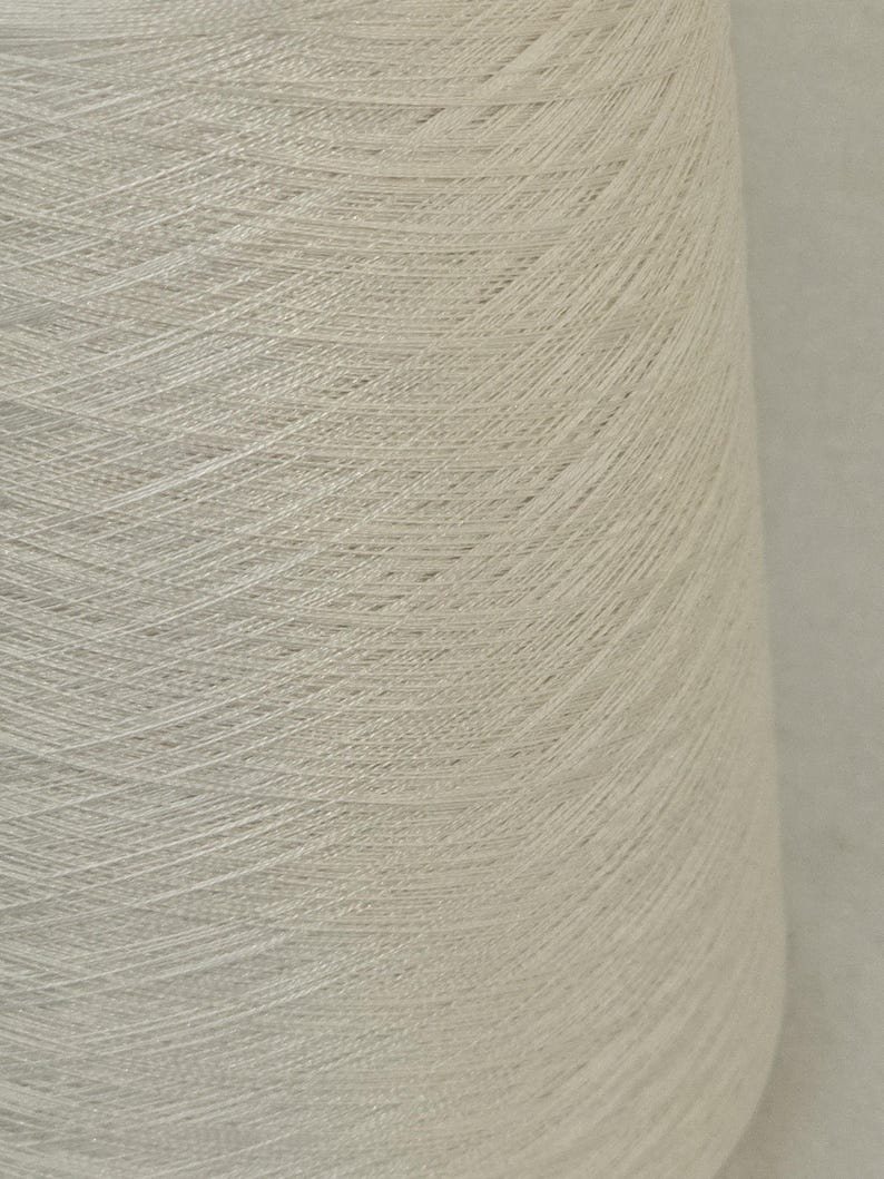 May include: A close-up of a spool of white yarn. The yarn is tightly wound and has a smooth, even texture.