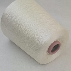 May include: A spool of white yarn with a slight sheen. The yarn is wound tightly and has a smooth texture.