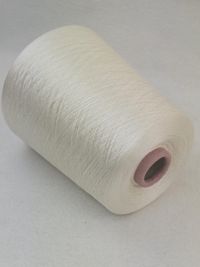 May include: A spool of white yarn with a slight sheen. The yarn is wound tightly and has a smooth texture.