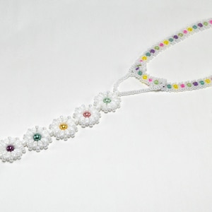 Pode incluir: Joias de pé de contas brancas com um bracelete de tornozelo de contas coloridas e uma corrente prateada. As joias de pé apresentam uma fila de contas brancas em forma de margarida com centros coloridos.