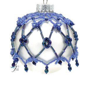 Puede incluir: Un adorno navideño blanco con una cubierta de cuentas azules e iridiscentes. Las cuentas forman un patrón geométrico con una franja colgante.