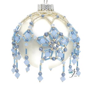 May include: A white Christmas ornament with a beaded design. The ornament features a star-shaped design in light blue and silver beads, with dangling beaded accents. The top has a silver metal cap and a hanging loop.
