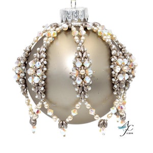 May include: A beaded Christmas bauble with a gold base and white and iridescent beads. The bauble has a beaded crown and a beaded fringe.