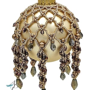 Puede incluir: Un adorno navideño dorado con cuentas, con un diseño delicado e intrincado y hebras de cuentas colgantes en tonos marrones y morados.