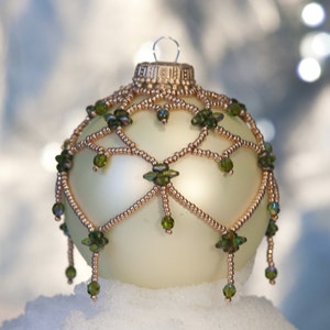 May include: A cream-coloured glass Christmas bauble with a gold beaded design and green glass beads hanging from the bottom.
