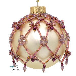 Puede incluir: Un adorno de Navidad de cuentas con una base dorada y un diseño de cuentas rosa y morado. El adorno tiene un patrón geométrico y está decorado con cuentas pequeñas.