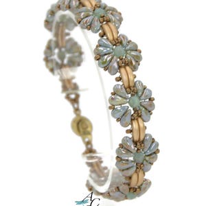May include: A beaded bracelet featuring a floral design. The bracelet has light blue and beige beads, with a gold-colored clasp. The floral elements are arranged in a repeating pattern. The bracelet is displayed against a white background.
