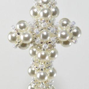 以下が含まれることがあります： 銀色のチェーンが付いた白いビーズの十字架のペンダント。十字架は小さな白い真珠と透明なビーズで作られています。