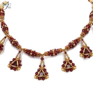 May include: A handcrafted necklace featuring a series of burgundy-colored crystal beads and gold-toned accents. The necklace has a central strand with dangling triangular pendants, each adorned with burgundy crystals and gold details. The design is intricate and elegant.