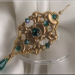 Puede incluir: Pendiente de aro dorado y verde con un cristal verde en forma de lágrima en la parte inferior.