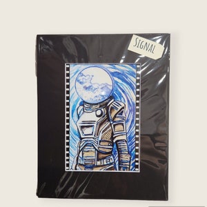 Può includere: Illustrazione di un astronauta con un casco a bolla trasparente, su uno sfondo blu a spirale. La tuta dell'astronauta è dettagliata in tonalità marroni e bianche. La parola "SIGNAL" è su una piccola etichetta.