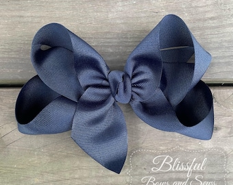 May include: A large navy blue hair bow with a simple, classic design. The bow is made from grosgrain ribbon and is tied in a double loop.