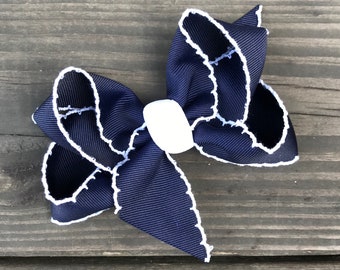 May include: A navy blue bow with white stitching around the edges. The bow is tied with a white center.