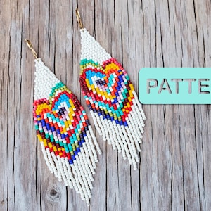 Könnte beinhalten: Ein Paar lange, weiße Perlenohrringe mit einem bunten Herzmuster. Die Ohrringe hängen an einer Holzoberfläche mit einem Schild, auf dem "PATTERN" steht.