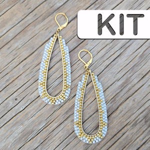 May include: Teardrop earrings with gold frames and lever-back clasps. The earrings feature a pattern of small, light blue and gold beads. The word "KIT" is displayed in a white rectangle. The earrings are a craft kit.