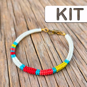 Peut inclure: Un bracelet en perles blanches avec des accents rouges, jaunes et bleus. Le bracelet a un fermoir doré et est étiqueté "KIT".