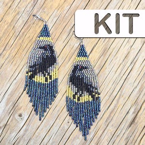 Peut inclure: Une paire de longues boucles d'oreilles triangulaires en perles représentant un corbeau noir sur une lune jaune et un ciel bleu foncé. Les boucles d'oreilles ont une frange de perles bleu foncé pendantes et des crochets argentés. Le texte KIT est visible.