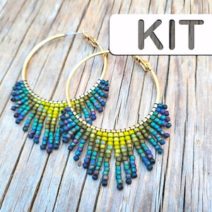 May include: Gold hoop earrings with a beaded fringe in shades of blue, green, and yellow. The word "KIT" is in a white rectangle in the upper right corner. The earrings are displayed on a wooden surface.