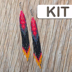 Peut inclure: Une paire de longues boucles d'oreilles perlées avec un design vibrant. Les boucles d'oreilles présentent un motif de perles rouges, noires, bleues et jaunes. Le mot "KIT" est affiché sur un rectangle blanc en arrière-plan. Les boucles d'oreilles sont posées sur une surface en bois.