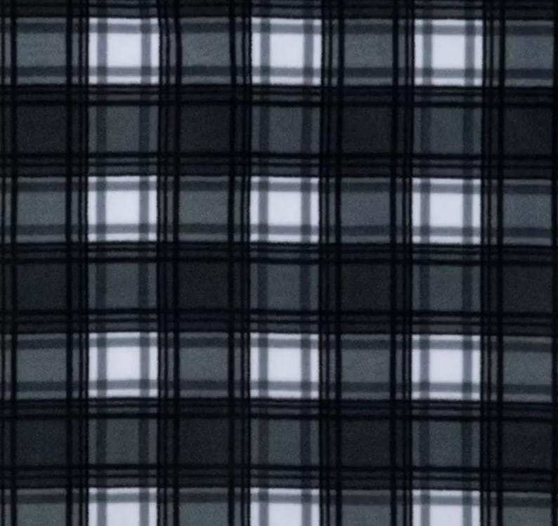 May include: A close-up of a plaid fabric pattern. The pattern features a grid of intersecting lines in black, dark gray, and light gray, creating a checkered design with white squares. The fabric appears to be soft and textured.