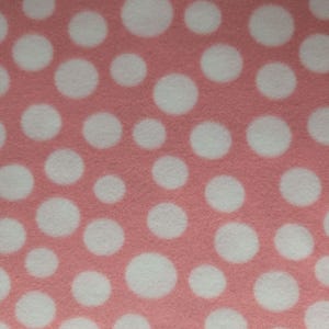 May include: Close-up of a pink fabric with a pattern of large, white polka dots. The dots are evenly spaced across the surface, creating a playful and visually appealing design. The fabric has a soft, textured appearance.