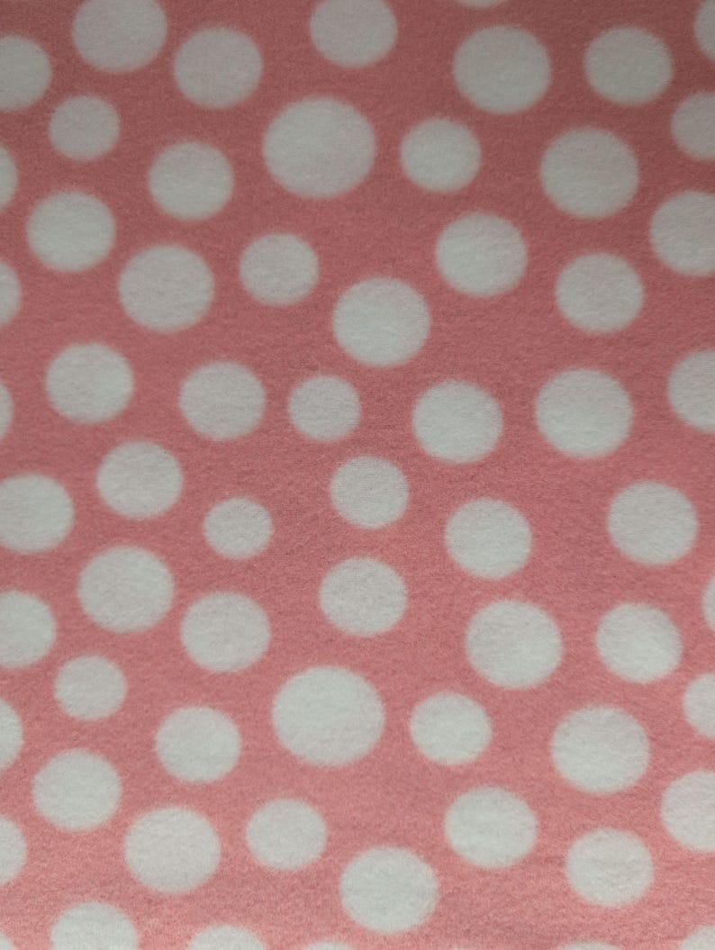 May include: Close-up of a pink fabric with a pattern of large, white polka dots. The dots are evenly spaced across the surface, creating a playful and visually appealing design. The fabric has a soft, textured appearance.