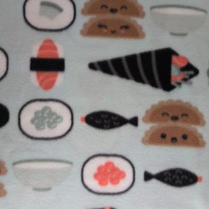 May include: A light blue fleece fabric featuring a repeating pattern of sushi rolls, nigiri, and other Japanese food items. The sushi pieces include salmon, rice, and seaweed, with some pieces having smiling faces.