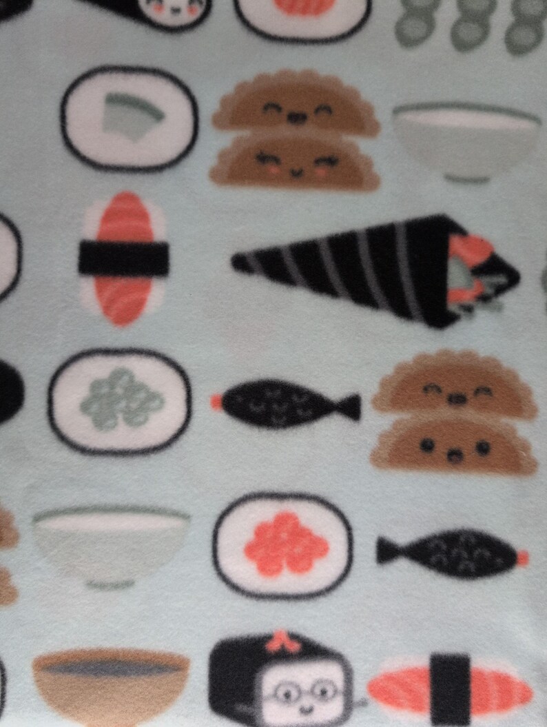 May include: A light blue fleece fabric featuring a repeating pattern of sushi rolls, nigiri, and other Japanese food items. The sushi pieces include salmon, rice, and seaweed, with some pieces having smiling faces.