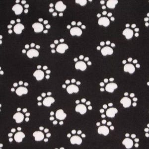 May include: Black fabric with a repeating pattern of white paw prints. The paw prints are scattered across the surface, creating a playful and whimsical design. The fabric appears to be soft and textured.