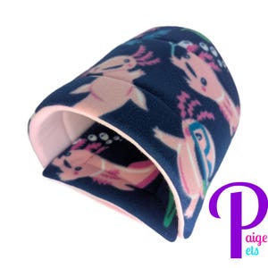 May include: A navy blue pet bed with a pink axolotl pattern. The interior is a soft pink. The bed is designed to provide a cozy and secure space for small pets. The logo "Paige's pets" is in the bottom right corner.