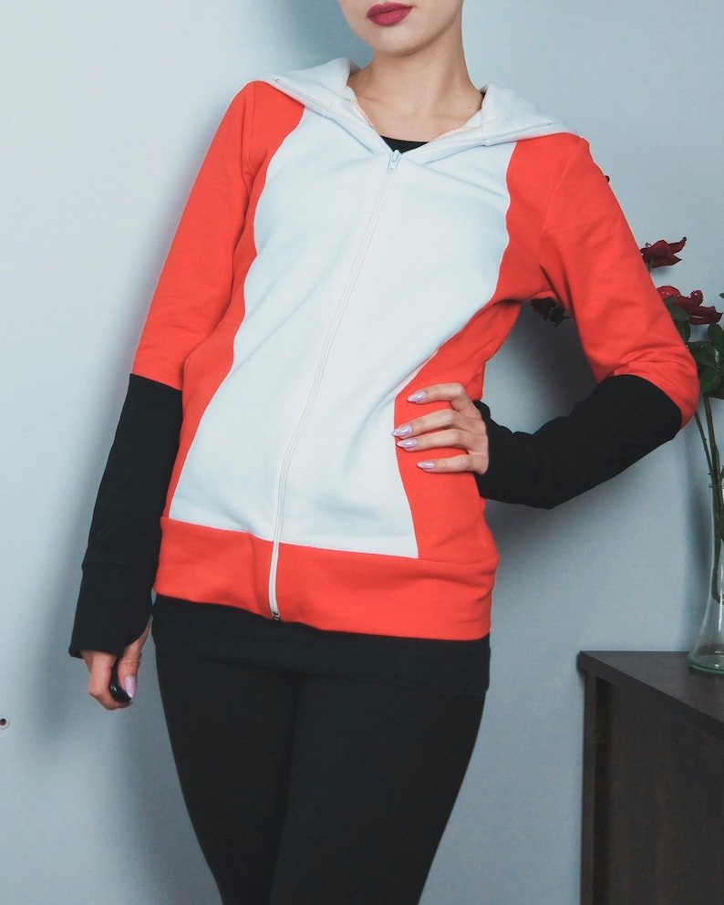 Puede incluir: Una sudadera con capucha roja, blanca y negra con cremallera. La sudadera tiene un panel blanco en la parte delantera y paneles rojos en los laterales.