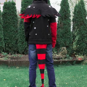 May include: A black hoodie with red and black wings and a long red and black tail. The hoodie has white polka dots and a zipper.