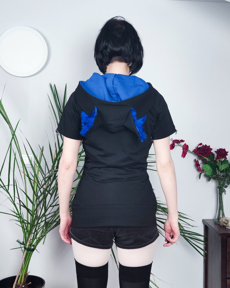 Puede incluir: Sudadera negra de manga corta con capucha azul y orejas de piel azul en la parte posterior.