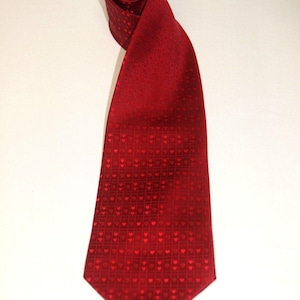 May include: A red tie with a repeating heart pattern. The tie is made of a shiny material and is rolled up at the top. The tie is a solid red color with a subtle pattern of small hearts.