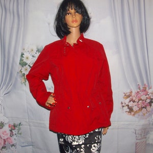 Puede incluir: Una chaqueta roja con cremallera, cuello alto y detalles plateados. La chaqueta tiene una silueta ajustada y mangas largas.