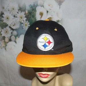 Puede incluir: Gorra de béisbol negra y dorada con el logotipo de los Pittsburgh Steelers. El logotipo es una estrella negra y amarilla con la palabra "Steelers" escrita en blanco.