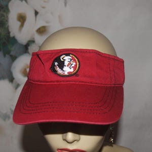 Peut inclure: Visière rouge avec bord cousu et un emblème circulaire avec un logo de tête de Seminole. La visière est faite d'un tissu durable et est conçue pour protéger les yeux du soleil.