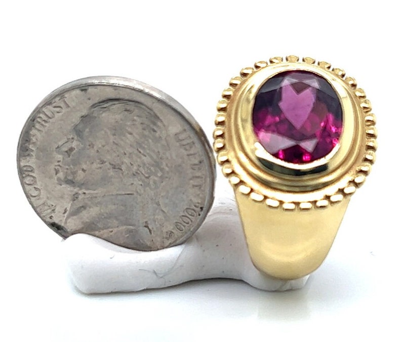 May include: A gold ring with a large oval-shaped pink gemstone set in a bezel setting. The ring is surrounded by a decorative border of small gold beads.