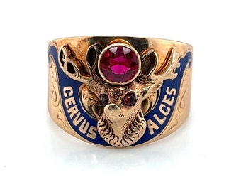 May include: A gold ring with a blue enamel band and a red gemstone. The band is engraved with the words "Cervus Alces" and features a detailed design of a deer head.